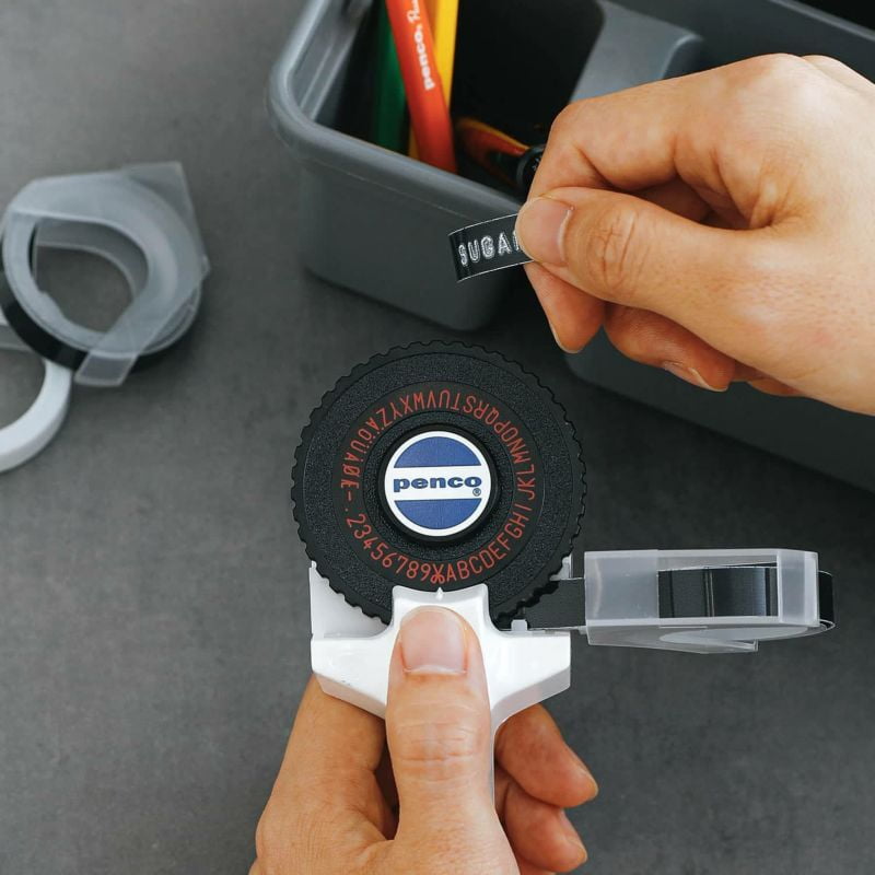 Penco Tape Writer labelmaker with black and white casing and printed tape loaded for creating custom labels.
