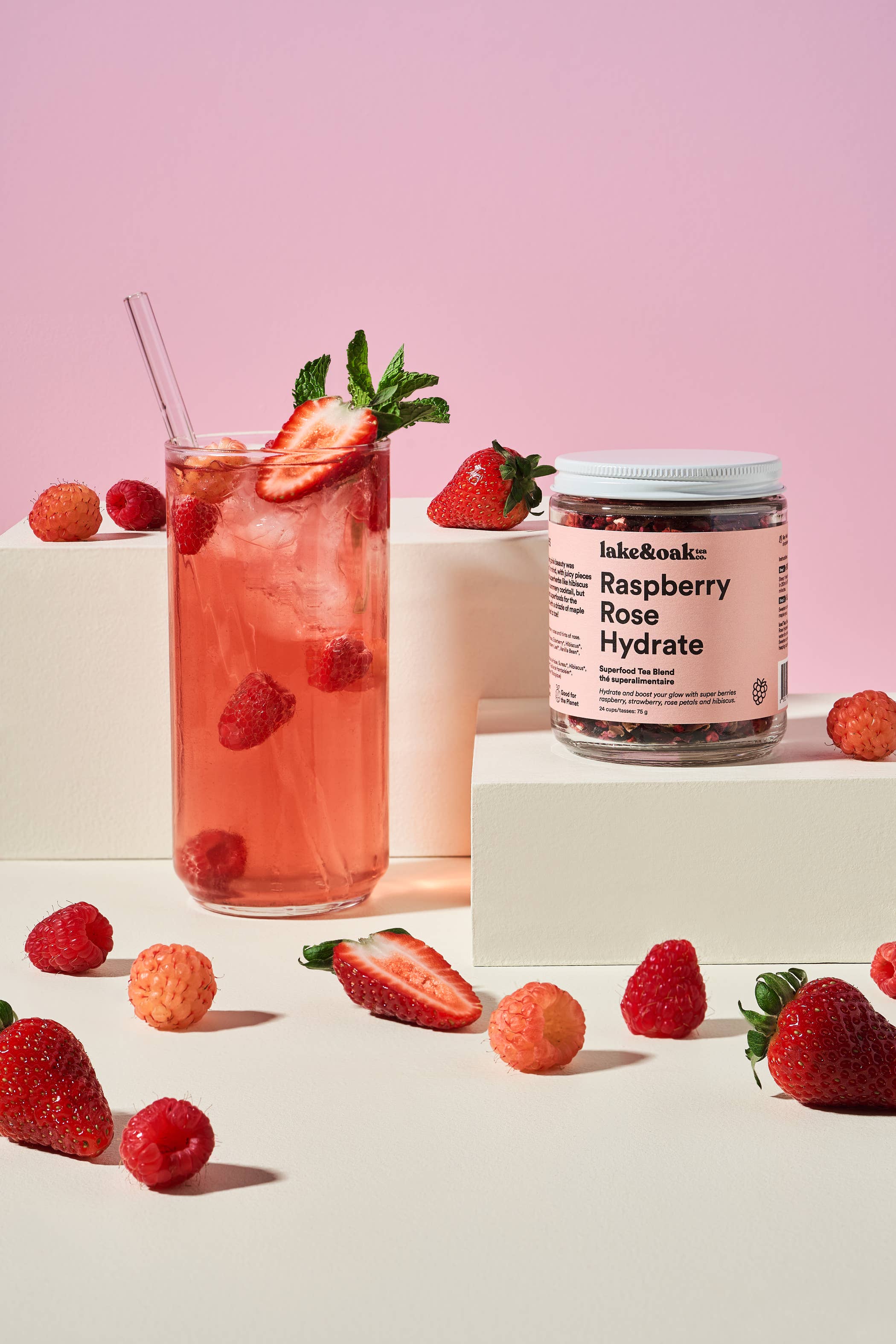 Raspberry Rose Hydrate tea by Lake & Oak Tea Co. in a glass cup with fresh raspberries and rose petals on a wooden table.