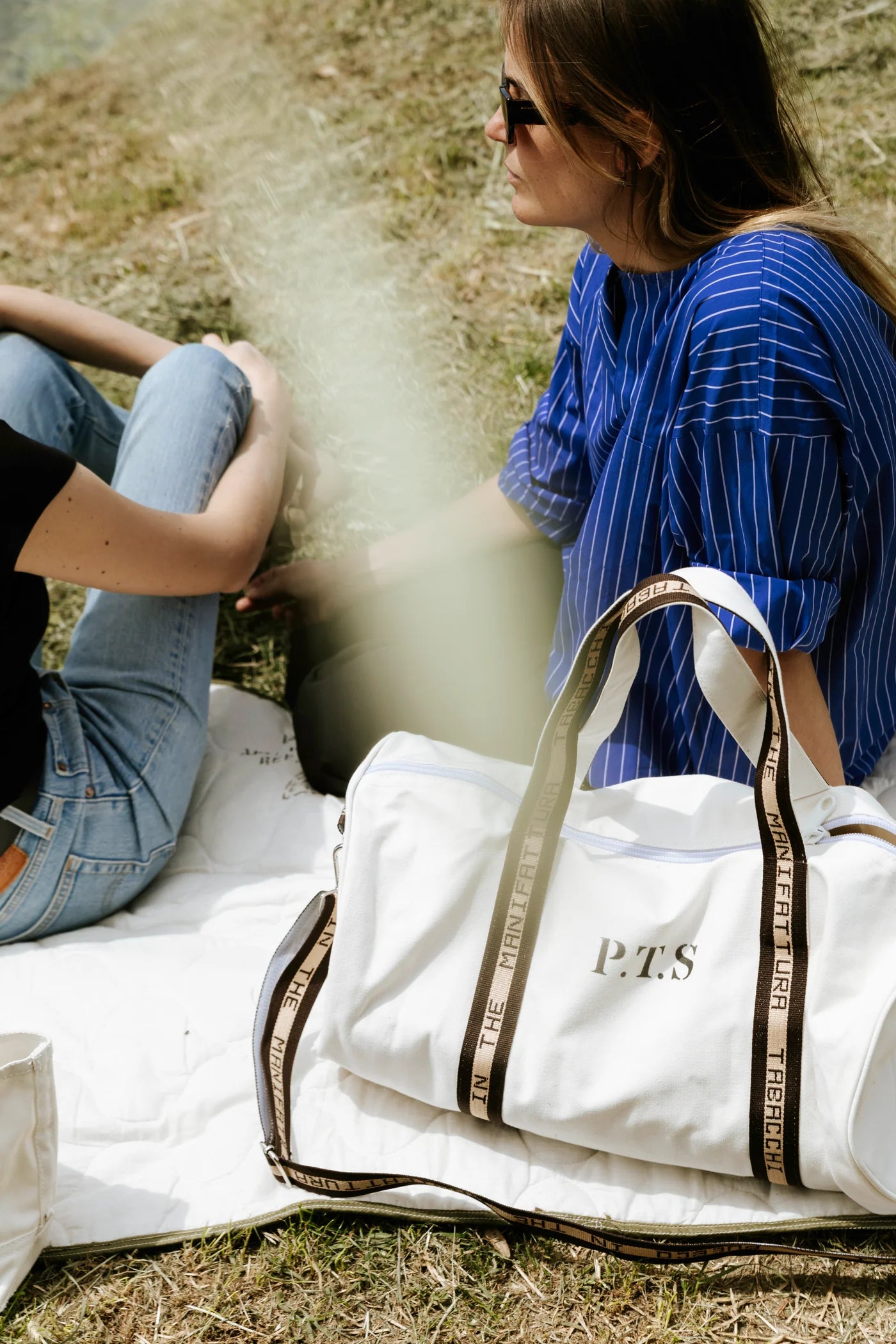Puebco barrel bag in natural canvas with leather accents, featuring a rounded shape and adjustable shoulder strap.