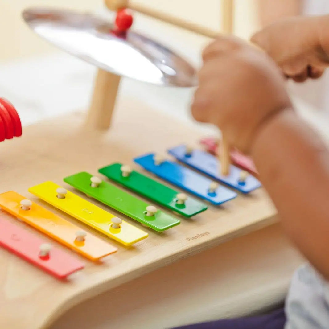 PlanToys Music Play toy with colorful wooden musical instruments and a child playing, promoting musical development and sensory fun.