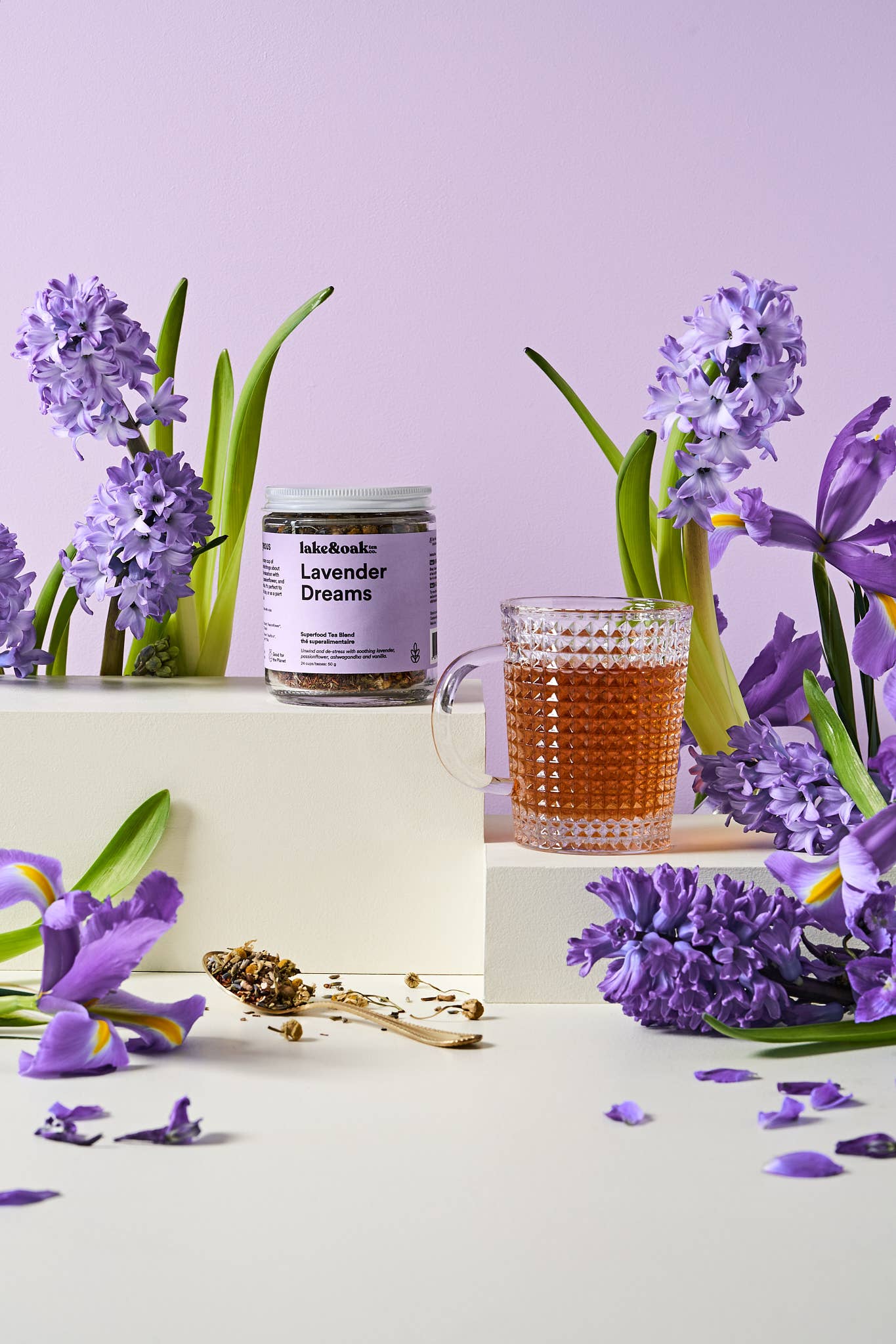 A cup of Lavender Dreams tea by Lake & Oak Tea Co. with dried lavender flowers and a teapot on a cozy wooden table.