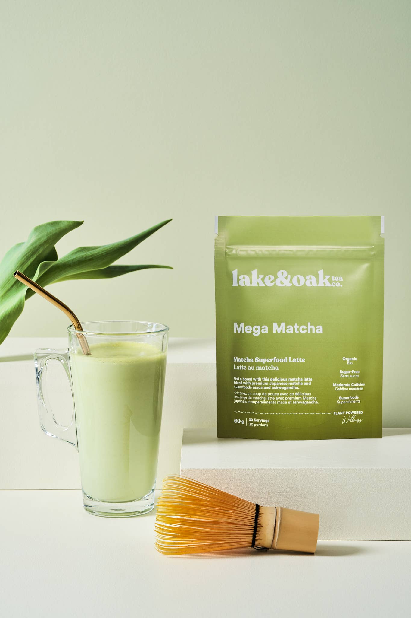 Loose Mega Matcha tea powder from Lake & Oak Tea Co. displayed in a clear glass bowl with a bamboo whisk on a wooden surface.
